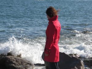 Imatge d'una dona mirant al mar amb les ones xocant a les roques. Imatge promocional de l'espectecle Paramo de la memòriaz
